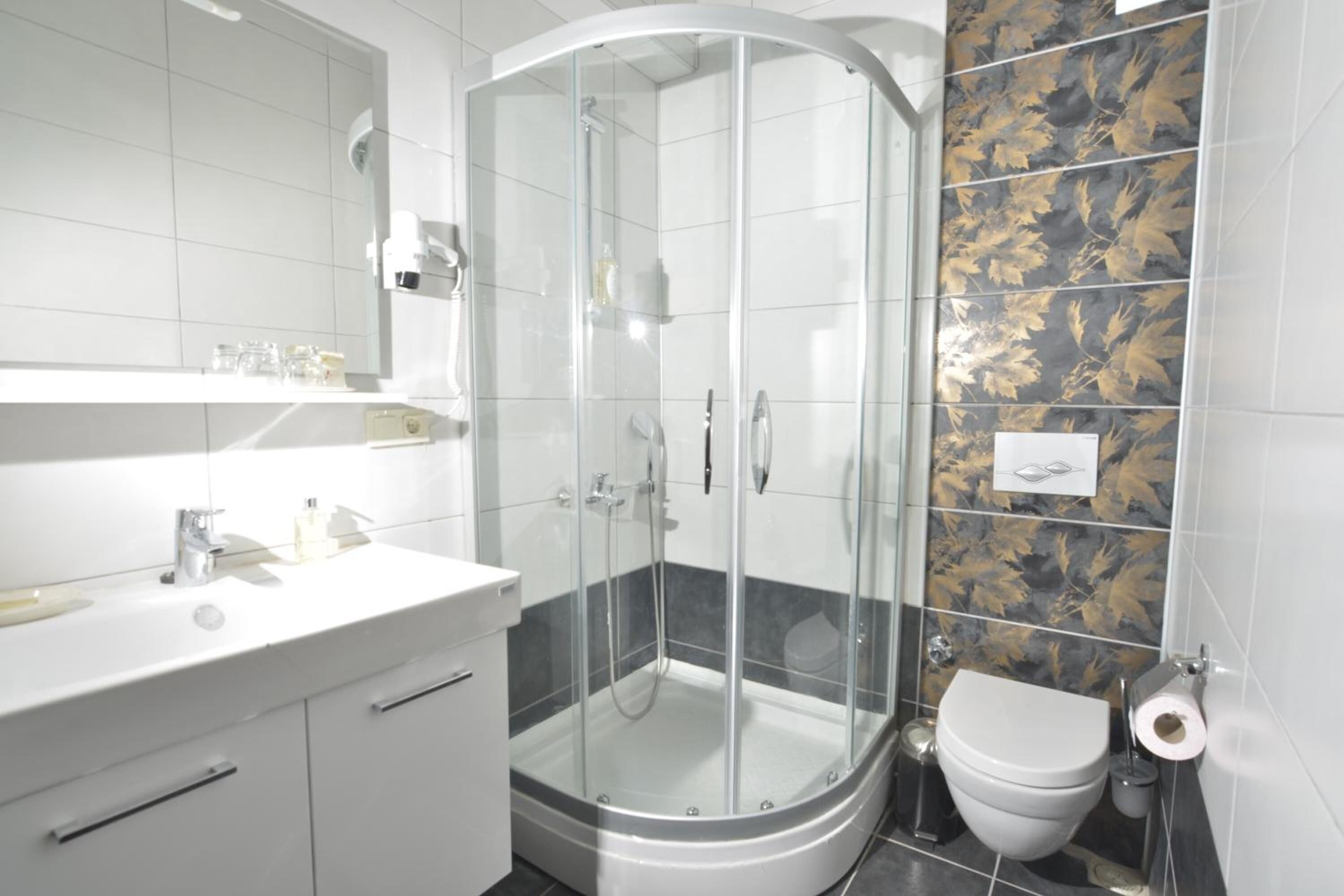 Un baño moderno con ducha de vidrio, lavamanos blanco y un inodoro.