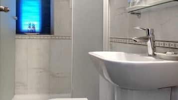 Une salle de bain avec des toilettes blanches, une douche et un lavabo surmonté d’un miroir.
