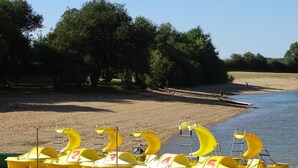A row of numbered yellow inflatable boats on a sandy beach with trees in the background. - Camping Parc de Charouzech (Salles-Curan)