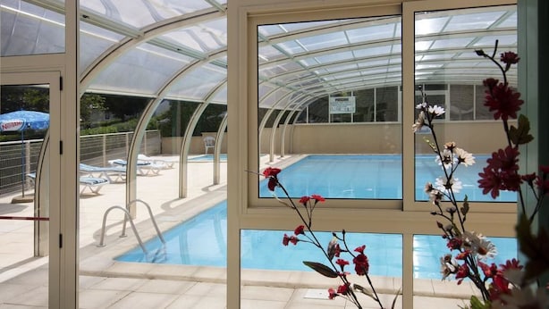 A pool area with a glass-enclosed structure, lounge chairs, and a clear view of the pool through the windows. - Camping Parc de Charouzech (Salles-Curan)