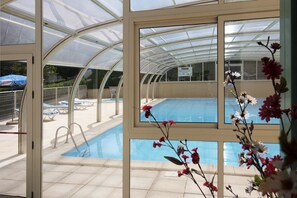 Et poolområde med en tilbygning i glas, liggestole og frit udsyn til poolen gennem vinduerne.