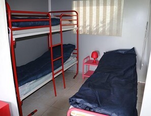 Een studentenkamer met stapelbedden, een klein bureau en een stoel.