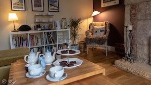 Ein gemütliches Wohnzimmer mit einem Couchtisch, der für Tee gedeckt ist, einem Bücherregal voller Bücher, einem Korbstuhl und gerahmten Bildern an der Wand.