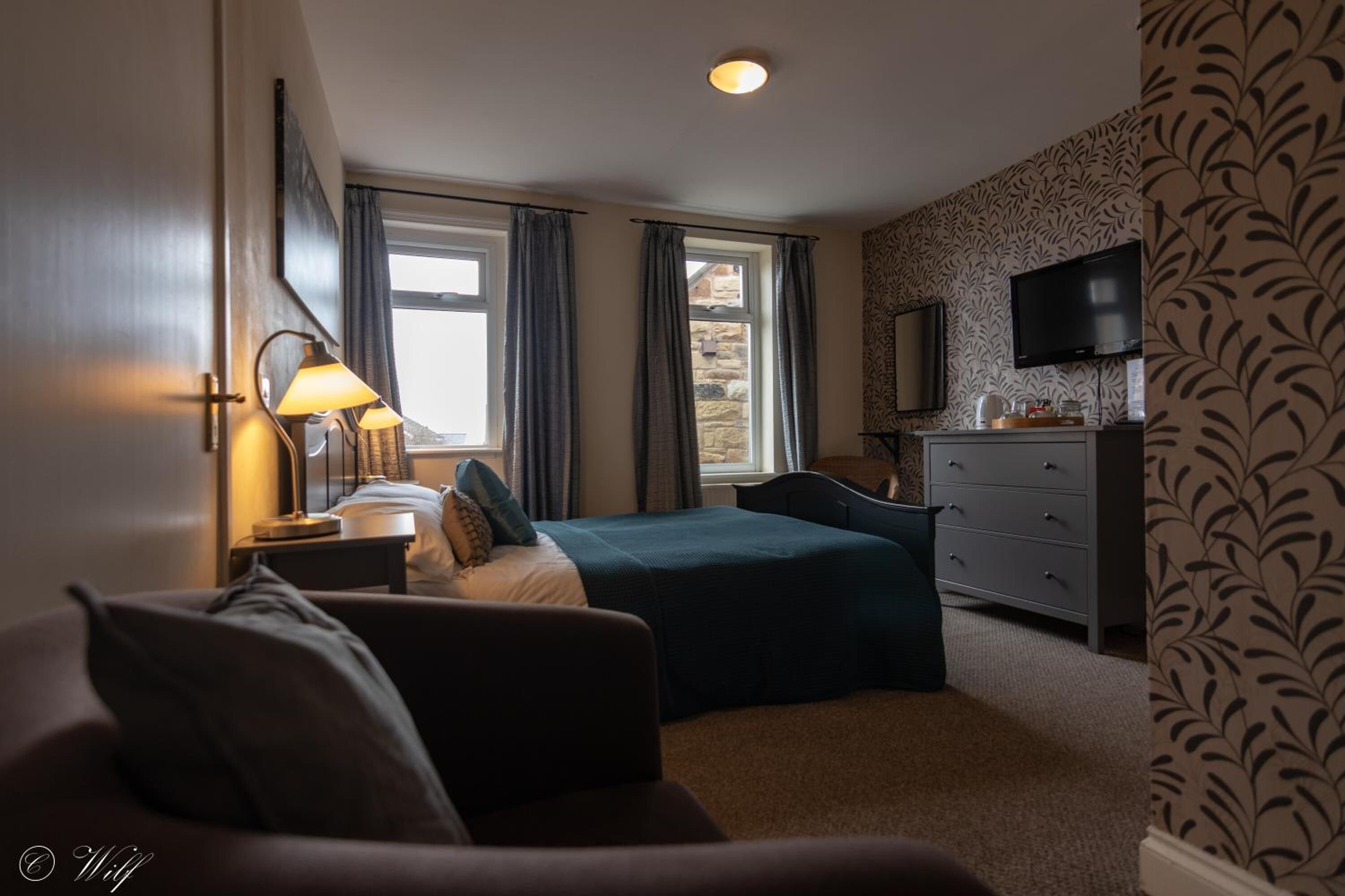 Una habitación de hotel con cama, escritorio, silla, televisión y ventana con cortinas.