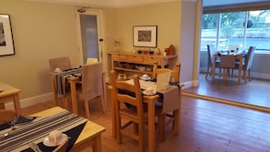 A cozy dining area with wooden furniture, a dining table set with plates and cutlery, and a window offering a view of the street.