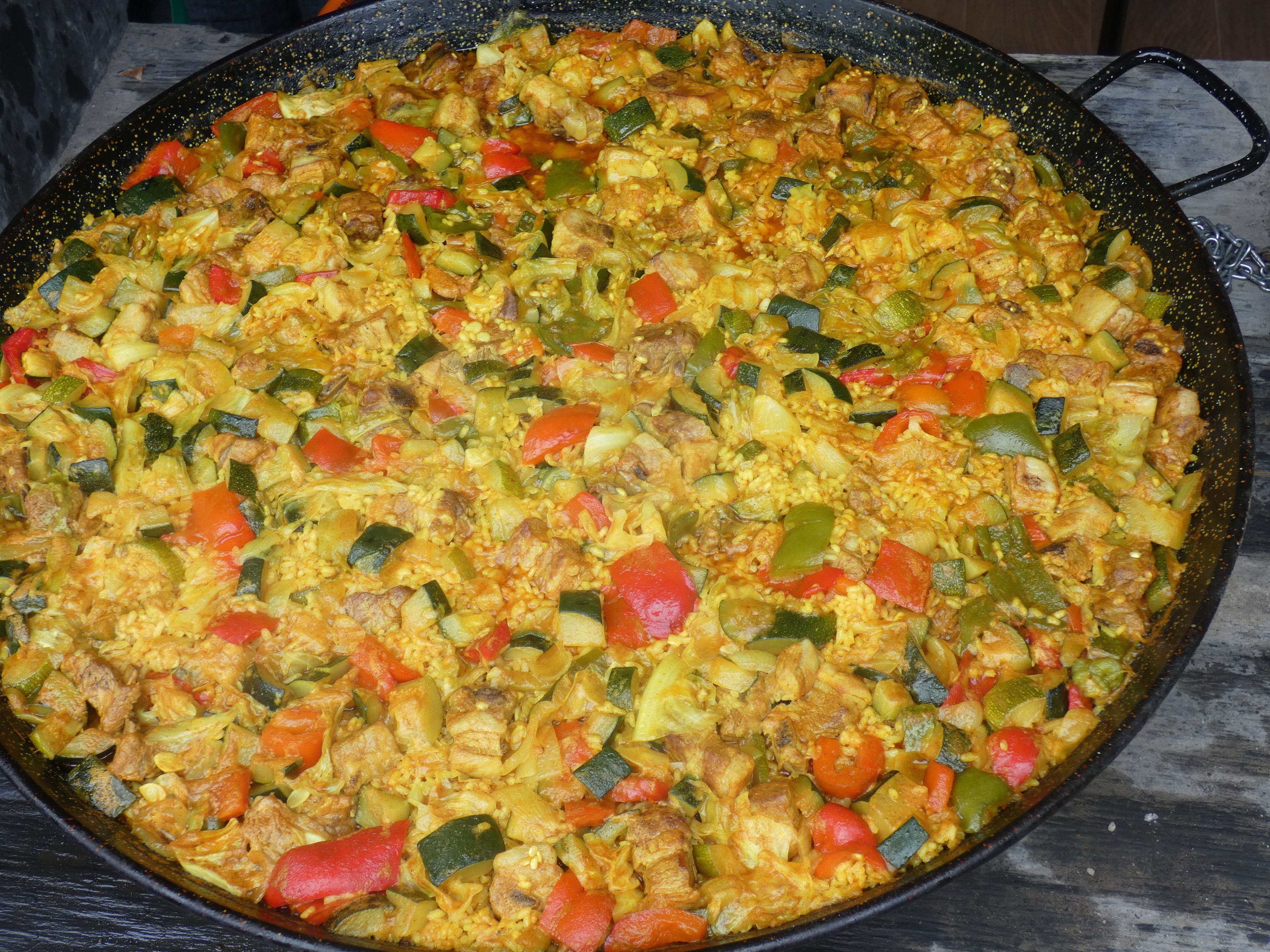 Une grande poêle ronde et noire, remplie d’un plat coloré à base de légumes et de riz.