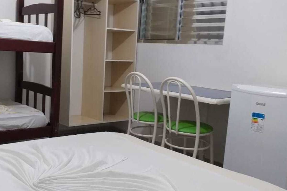 A bunk bed room with a desk and chair, a small refrigerator, and a window with blinds.