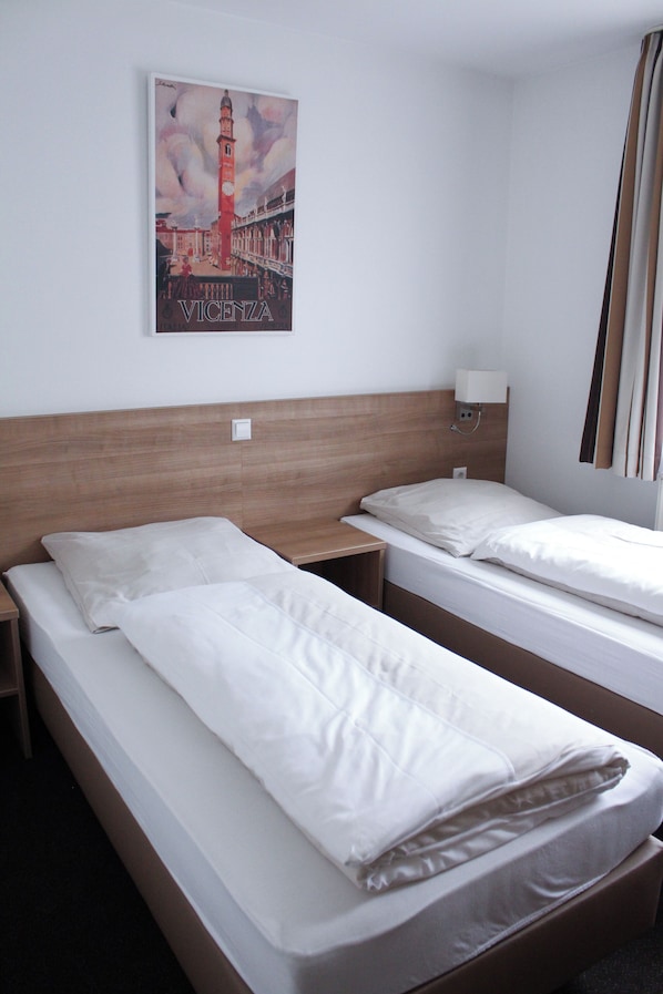 Habitación de hotel con dos camas individuales, cabecera de madera, mesita de noche, lámpara de pared y un cartel con un puente.
