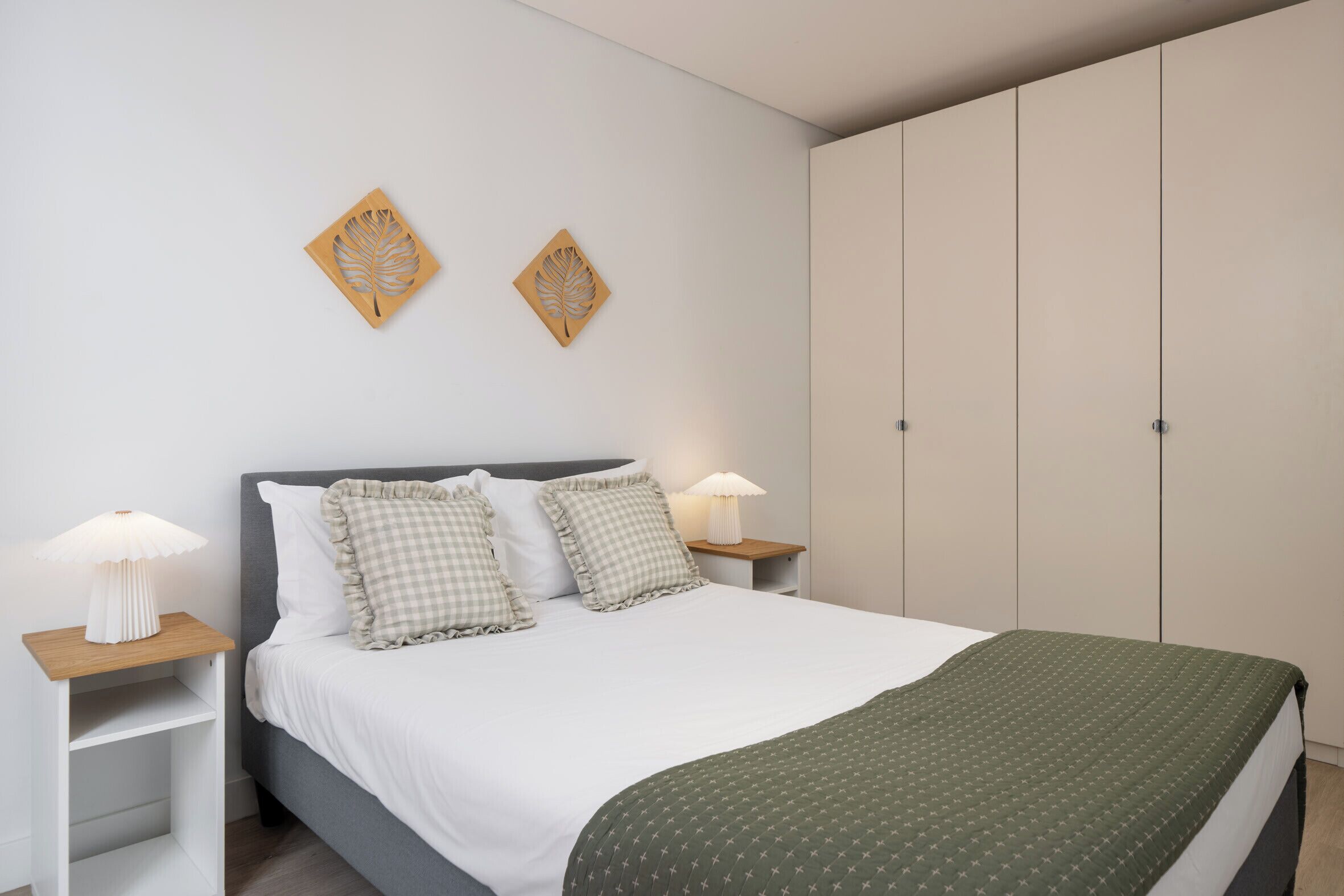A bedroom with a bed, two nightstands, a bedside lamp, a green blanket, and a wardrobe.
