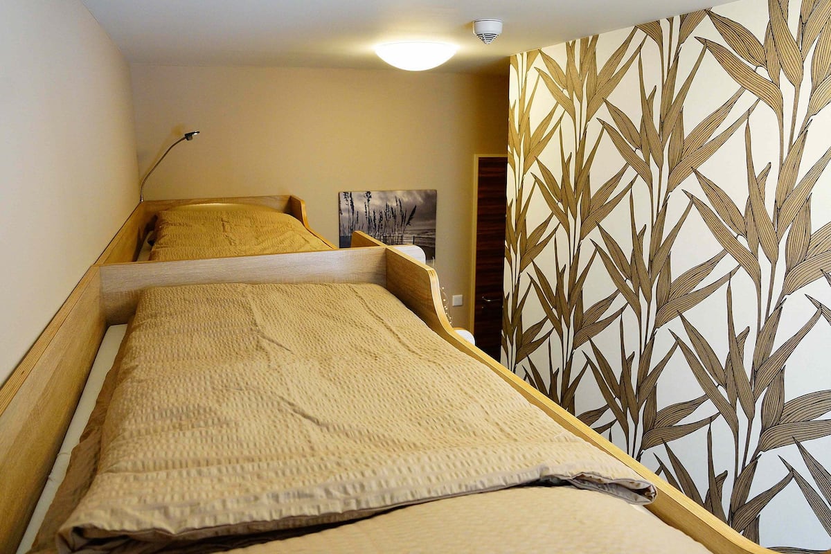 A narrow room with a bed, a wall-mounted security camera, and a door with a plant pattern.