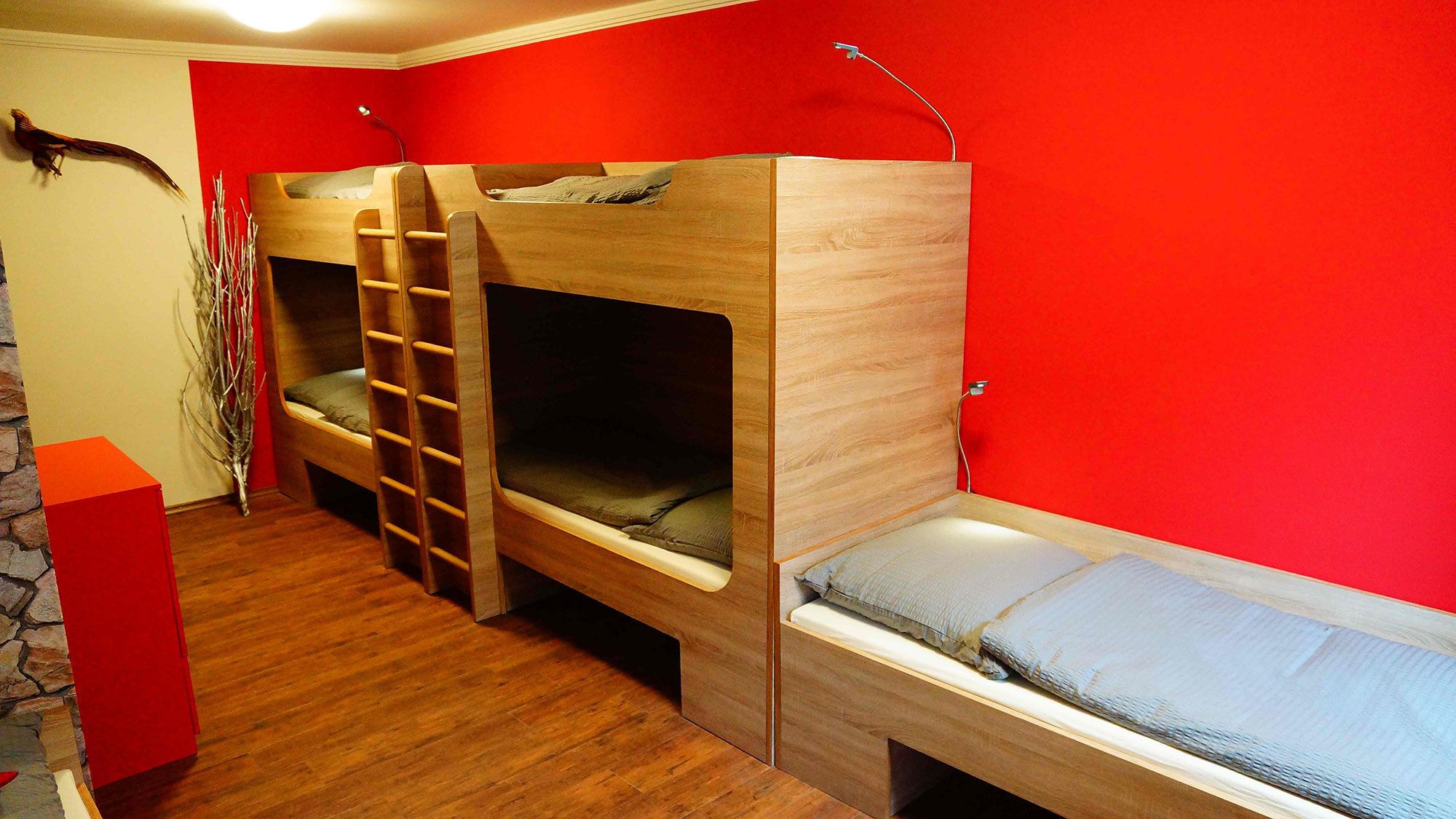 A room with a bunk bed, a small desk, and a red wall.