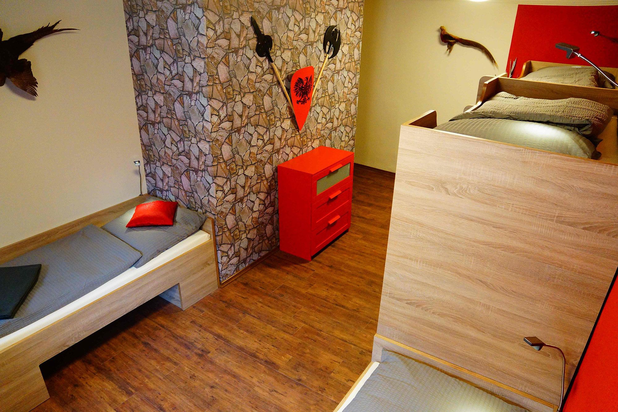 Un dormitorio con pared de piedra, cama con unidad de almacenamiento roja y cómoda de madera.