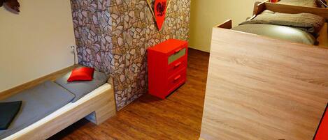 Un dormitorio con pared de piedra, cama con unidad de almacenamiento roja y cómoda de madera.
