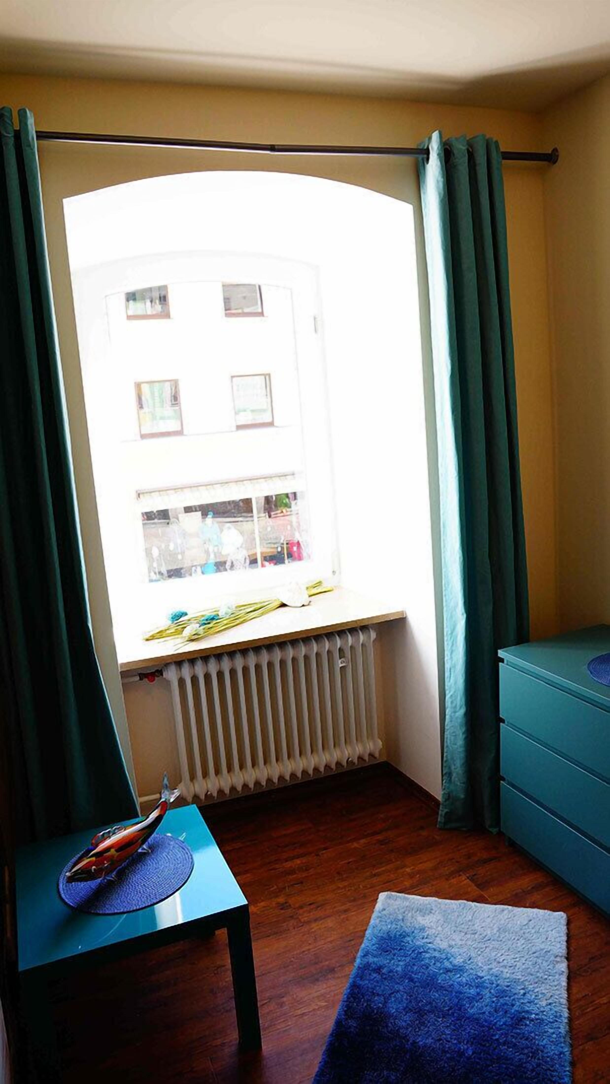A room with a window, a radiator, a blue table, and a blue sofa.
