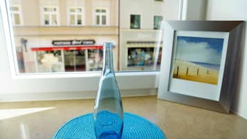 A clear view of a bottle on a blue mat, a framed picture of a beach, and a window with a view of buildings and a store.