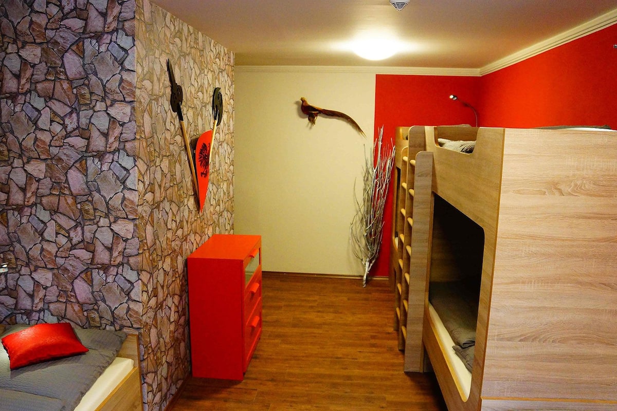 A room with a stone wall, a red cabinet, a bunk bed, and a wooden floor.