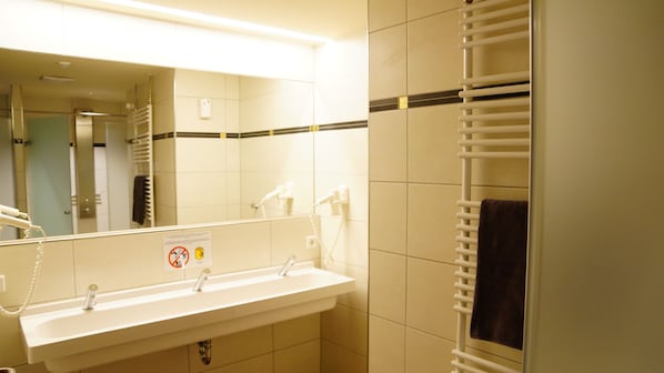 Un baño con lavamanos, espejo, toallero y un cartel de prohibido fumar.