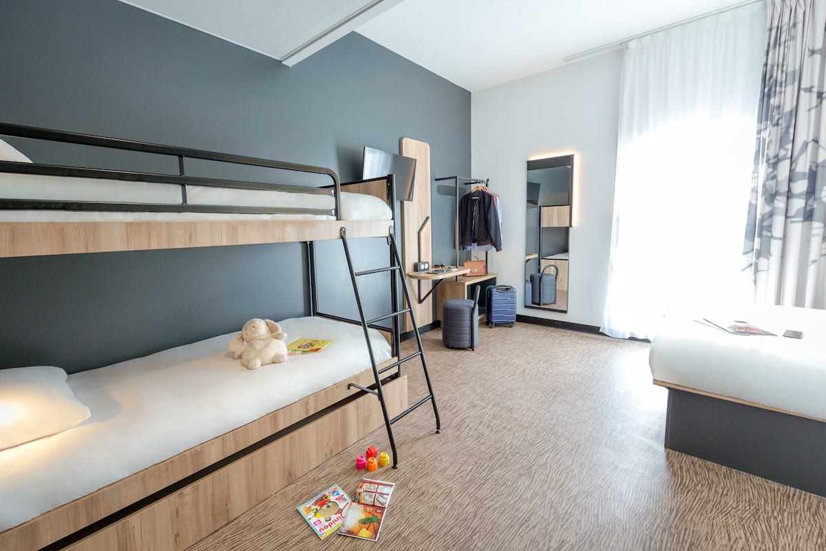 Ein modernes Hotelzimmer mit Etagenbett, Schreibtisch, Spiegel und einem Fenster mit Vorhängen.