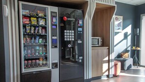 A vending machine with a variety of snacks and drinks, a coffee machine, and a small seating area with a couch and a table. - B&B HOTEL SAINTE MAXIME Golfe de St Tropez (4628) (Sainte-Maxime)