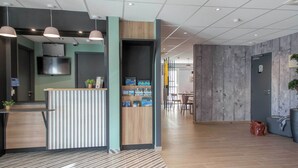 A modern reception area with a wooden counter, a flat-screen TV, and a seating area with a table and chairs. - B&B HOTEL SAINTE MAXIME Golfe de St Tropez (4628) (Sainte-Maxime)
