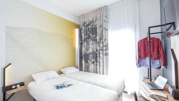 Habitación de hotel con dos camas, un escritorio con una computadora portátil, un perchero con chaquetas y un diseño de pared moderno.
