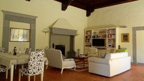 A living room with a fireplace, a television, a bookshelf, and a dining area with a table and chairs. - Pian dei Giullari Suite (Florence)