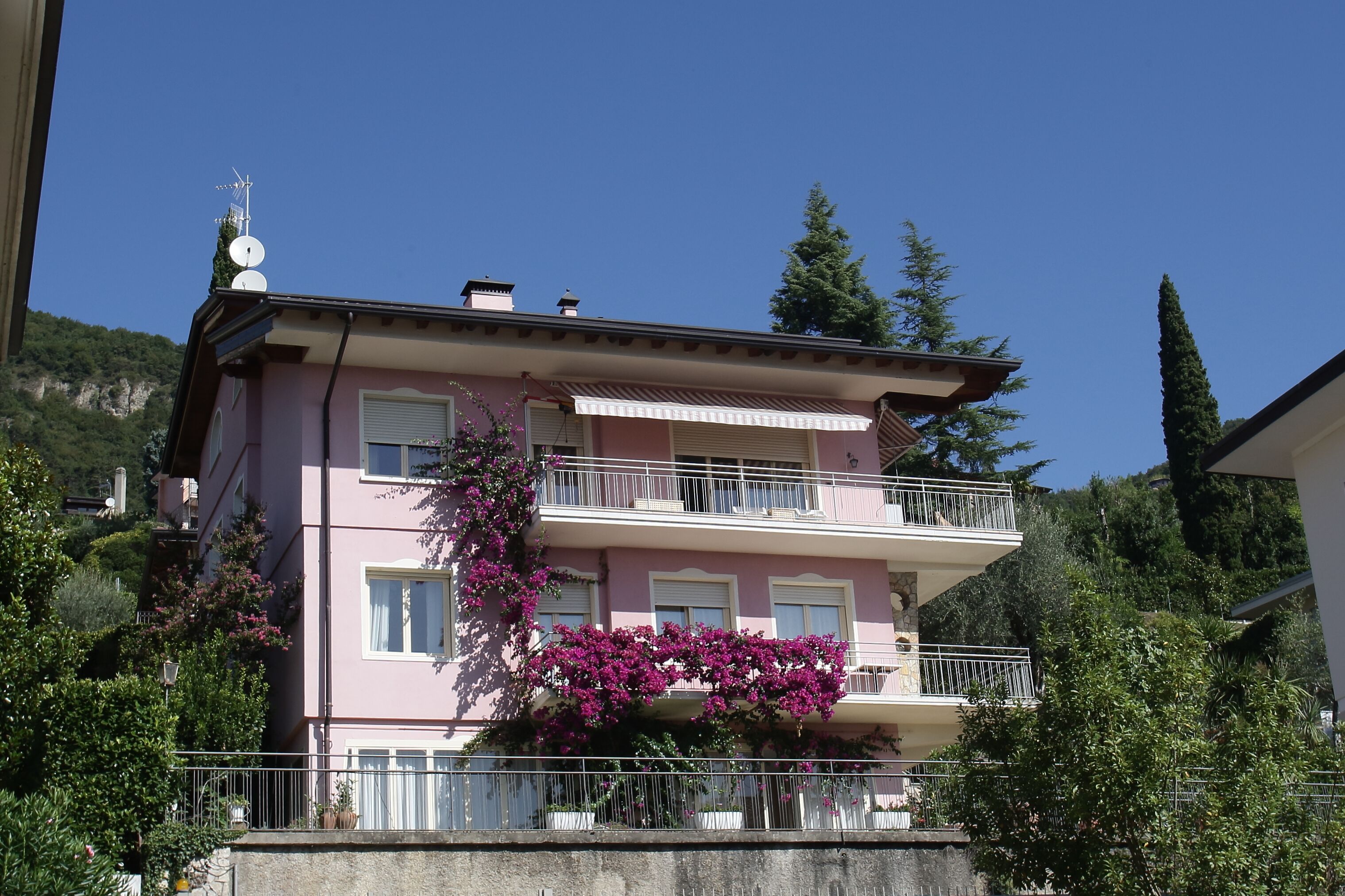 A pink multi-story building with balconies, surrounded by greenery and trees.