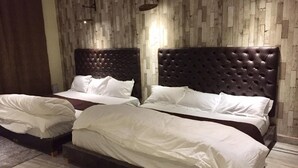 A hotel room with two beds, each with a tufted headboard, white bedding, and a wooden floor. - Rooming House (Greater Noida)