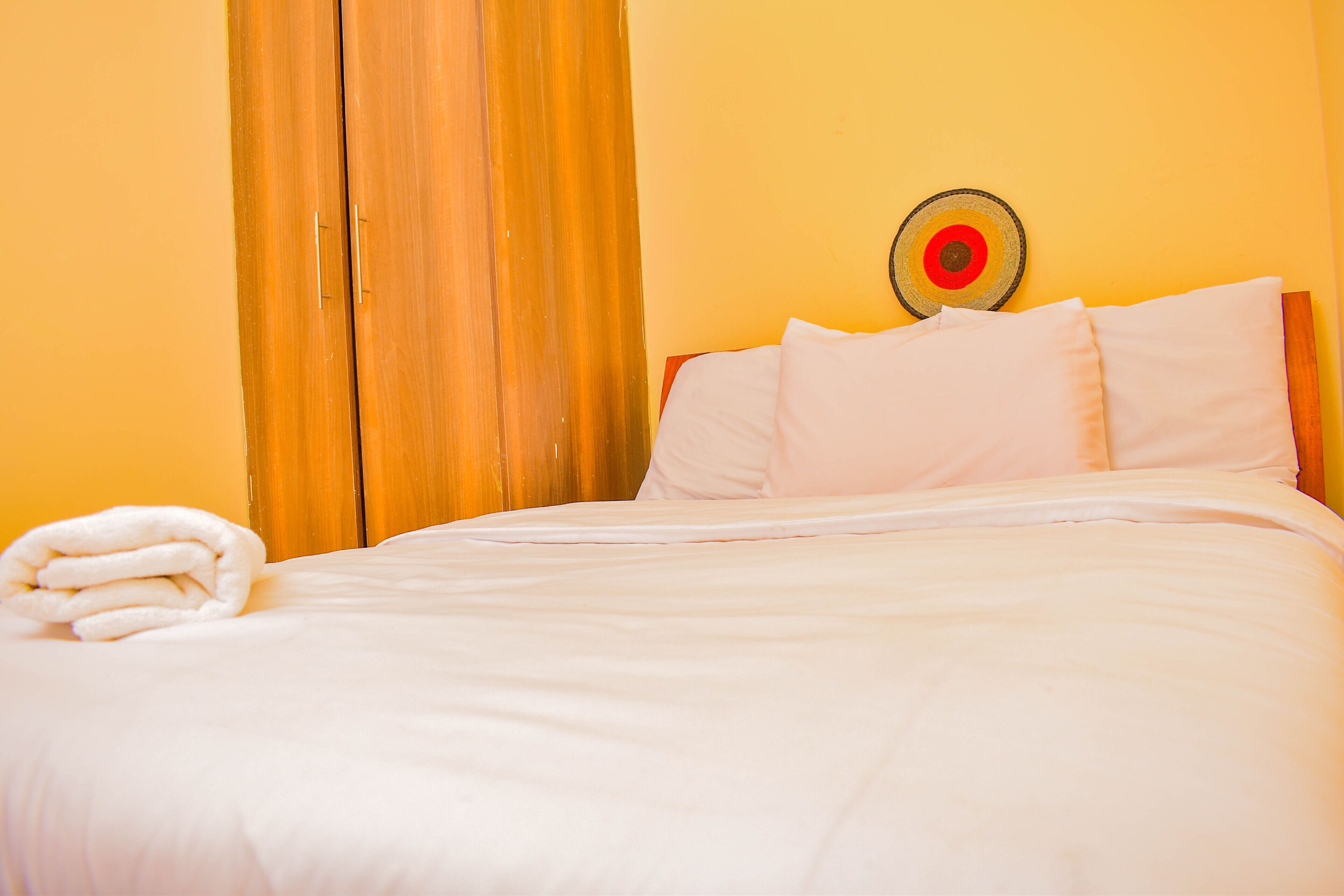 Cama bem arrumada com roupa de cama e almofadas brancas, cabeceira de madeira e um objeto decorativo na parede.