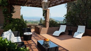 An outdoor patio with wicker furniture, a table with fruit, and a view of the city and mountains. - Antico Castello Marignolle (Florence)