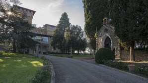 A paved pathway leading to a stone building with an arched entrance, surrounded by greenery and trees. - Antico Castello Marignolle (Florence)