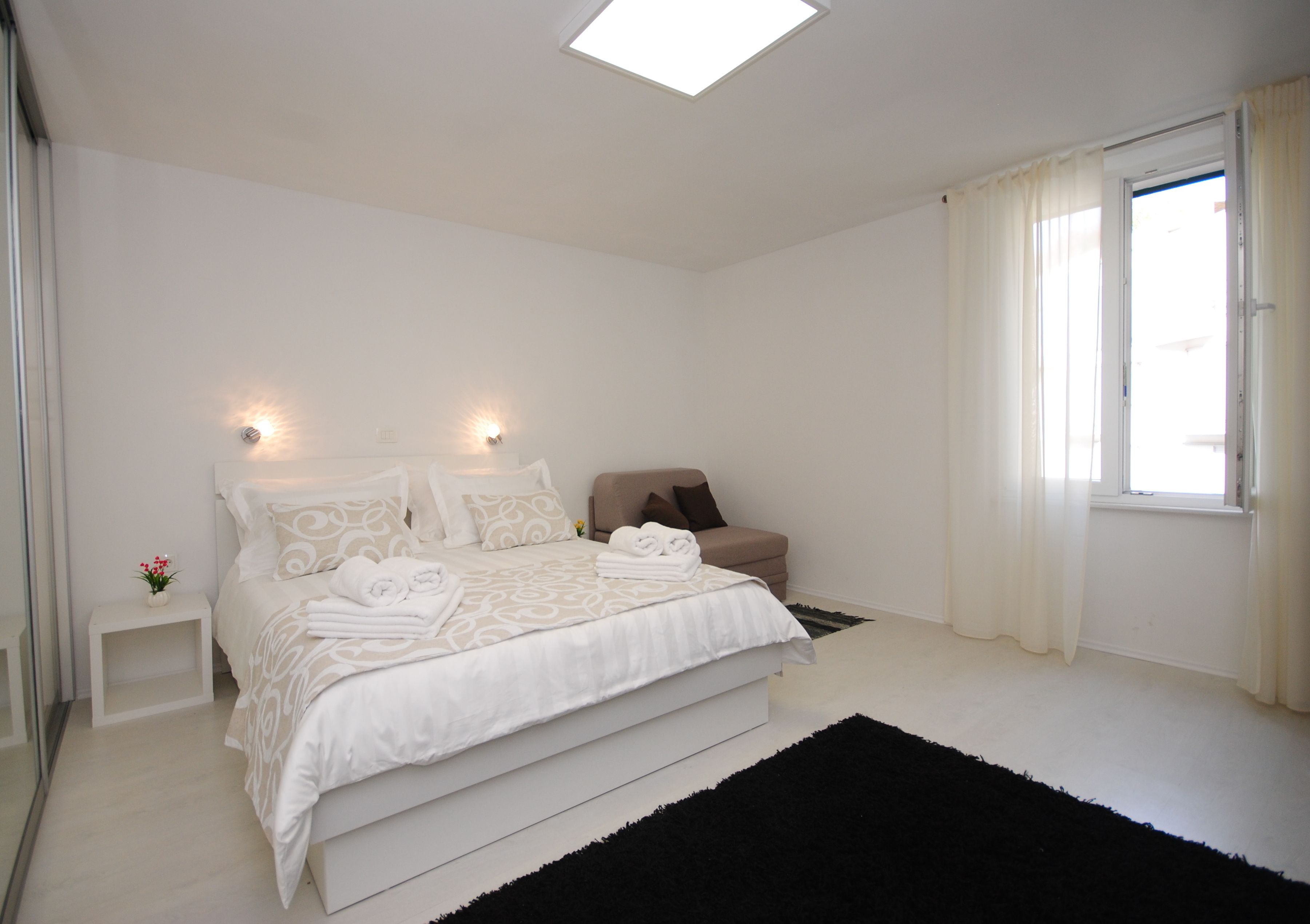Une chambre moderne avec un grand lit, des tables de chevet, une fenêtre avec des rideaux et un puits de lumière.