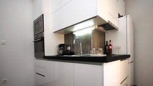 A modern kitchen with white cabinets, a black countertop, a built-in oven, a coffee maker, a sink, and a refrigerator.