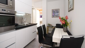 A modern kitchen with stainless steel appliances, a dining area with a table and chairs, and a vase with flowers on the wall.