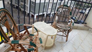 A balcony with two wicker chairs and a small table, a tiled floor, and a view of a residential area. - Cafri Homestay (Syokimau)