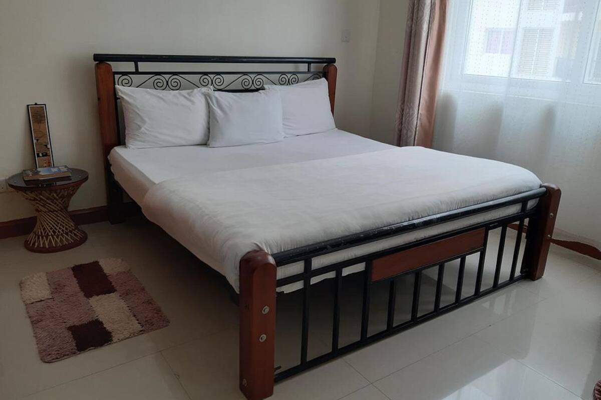 A neatly made bed with white linens in a room with a tiled floor and a small rug.