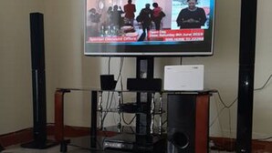 A flat-screen TV mounted on a wooden stand with a speaker on each side. - Cafri Homestay (Syokimau)
