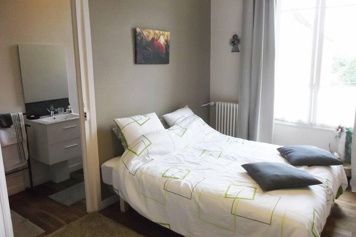 Ein Schlafzimmer mit Bett, Nachttisch, Spiegel, Heizkörper und einem fenster mit Vorhängen.