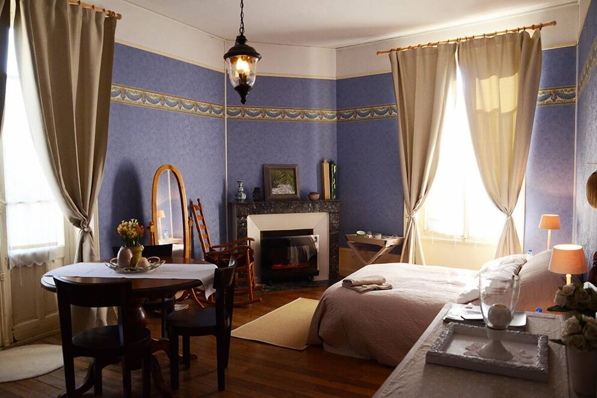 Ein Zimmer mit Kamin, einem Bett, einem Esstisch mit Stühlen und einer Chandelieber.