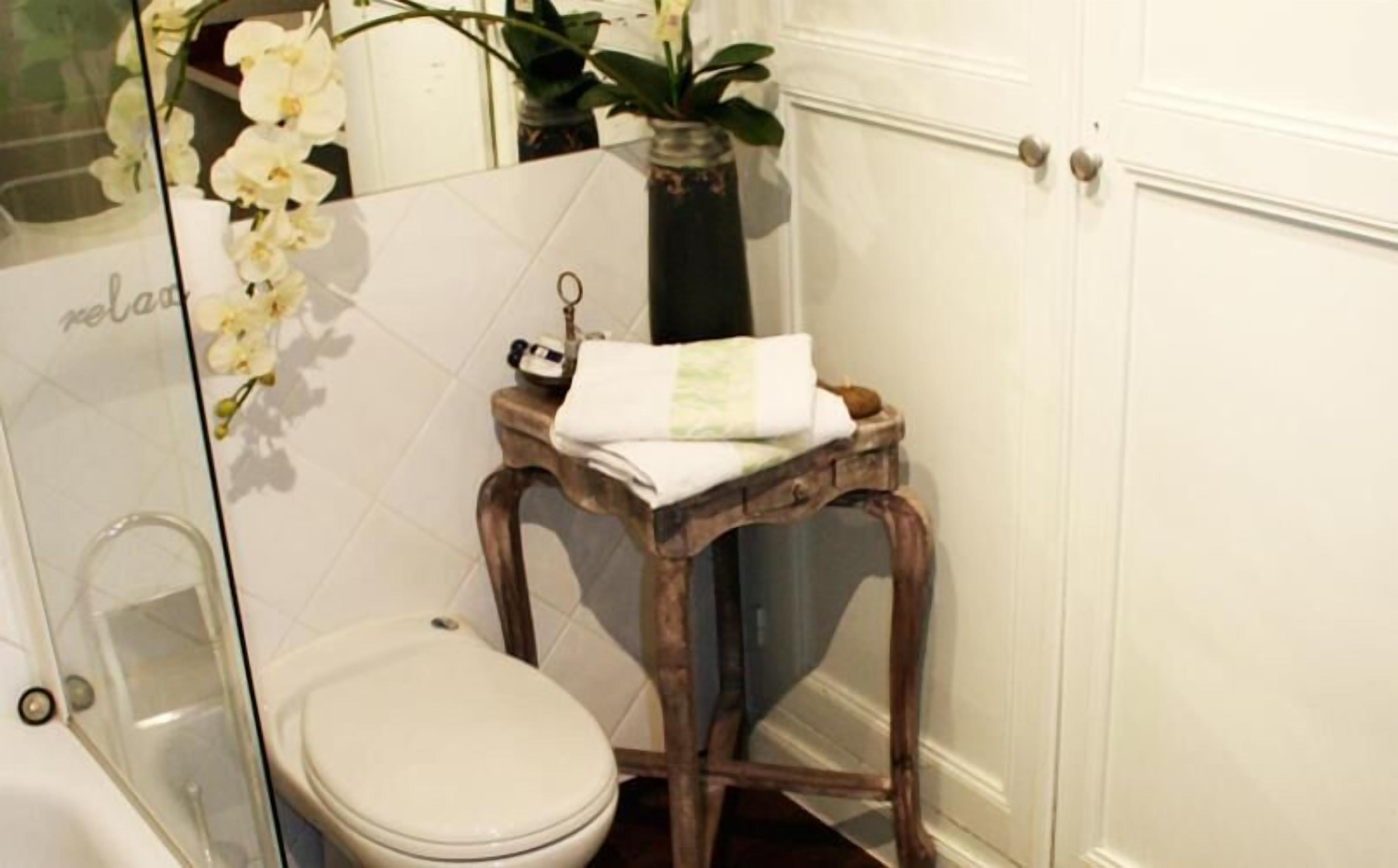 A bathroom with a white toilet, a wooden stool, a glass shower enclosure, and a potted plant.
