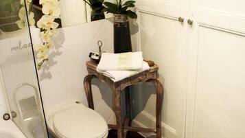 A bathroom with a white toilet, a wooden stool, a glass shower enclosure, and a potted plant.