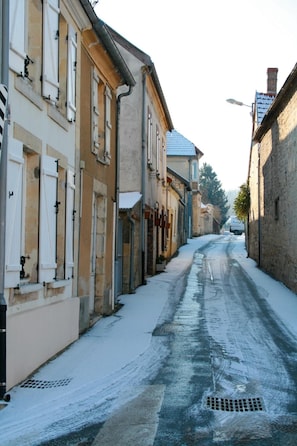 Une rue étroite bordée d’immeubles, dont certains sont dotés de volets, et un sol recouvert de neige.