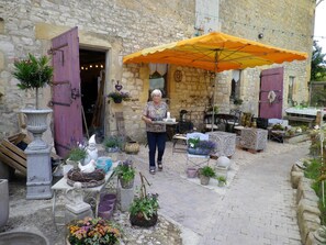 A stone building with an open door, outdoor seating area, and various potted plants.