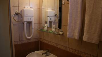 Casa de banho com lavatório, dois secadores de mãos, prateleira de vidro com produtos de higiene e porta-toalhas com duas toalhas.
