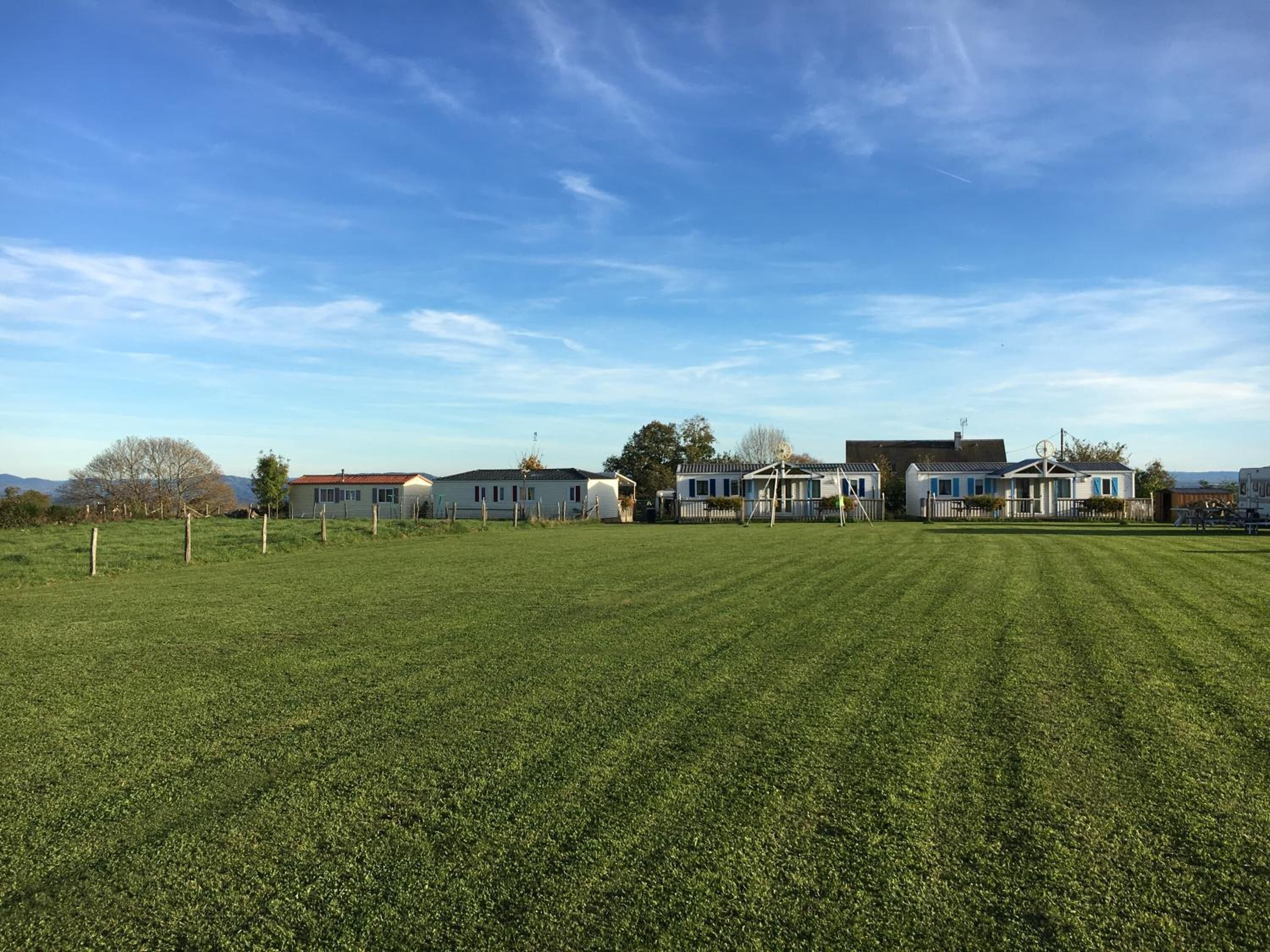 A row of mobile homes with a large grassy field in the foreground.