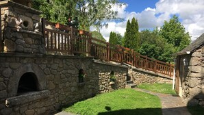 Un pont en pierre doté d’une rambarde en bois, menant à un bâtiment en pierre surmonté d’une cheminée.