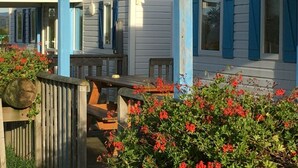 Une maison avec un porche, des volets bleus et un jardin orné de fleurs rouges.