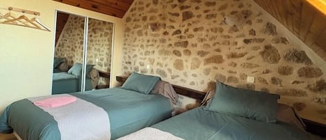 A bedroom with two beds, wooden ceiling, stone wall, and a mirror.