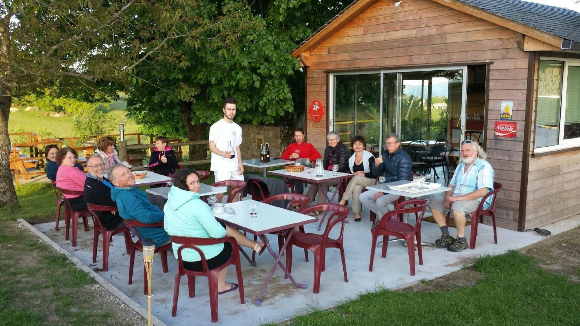 An outdoor seating area with tables and chairs, a wooden building with a glass door, and a Coca-Cola sign.