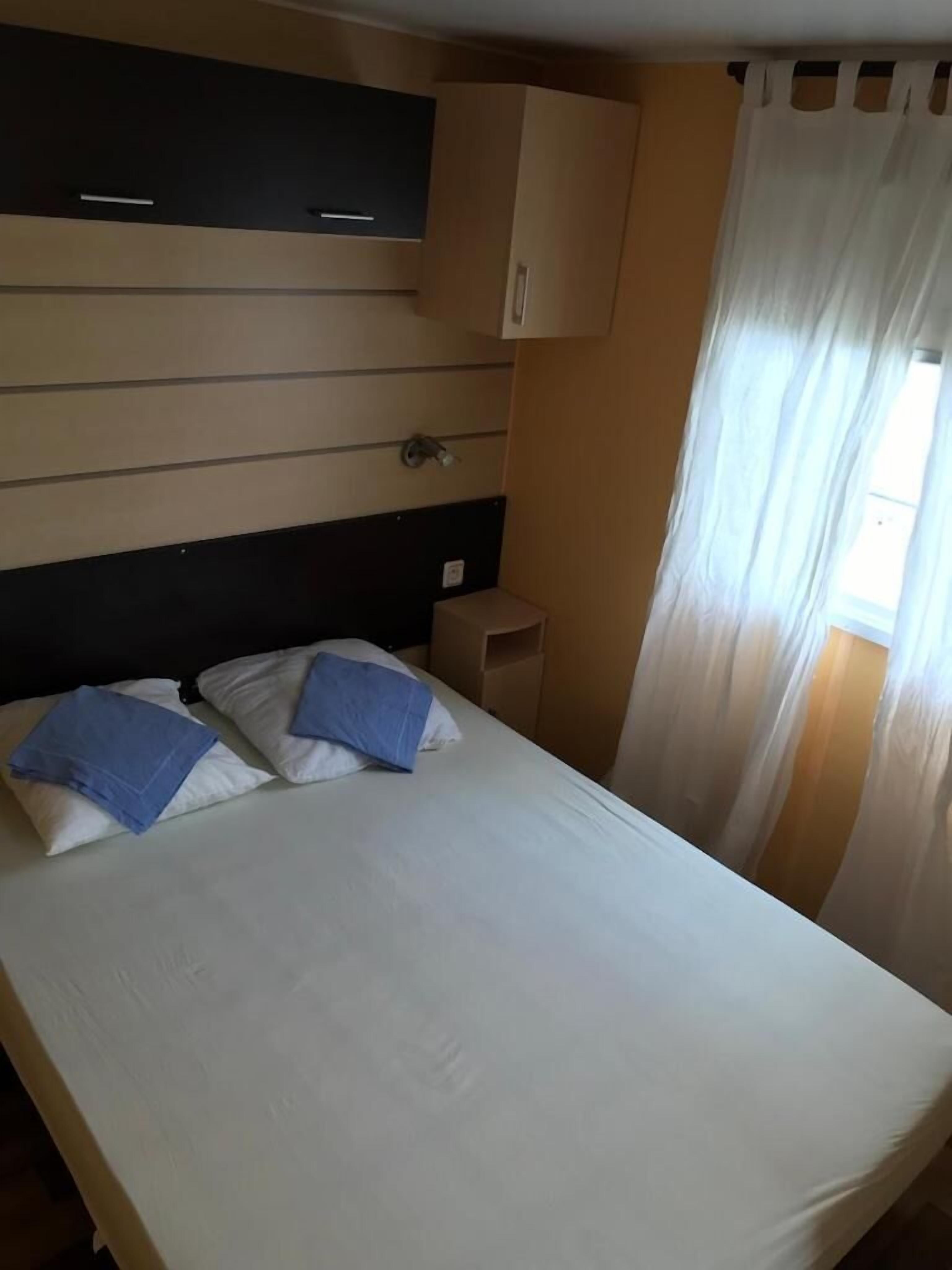 Habitación de hotel con cama, almohadas, mesita de noche y ventana con cortinas.